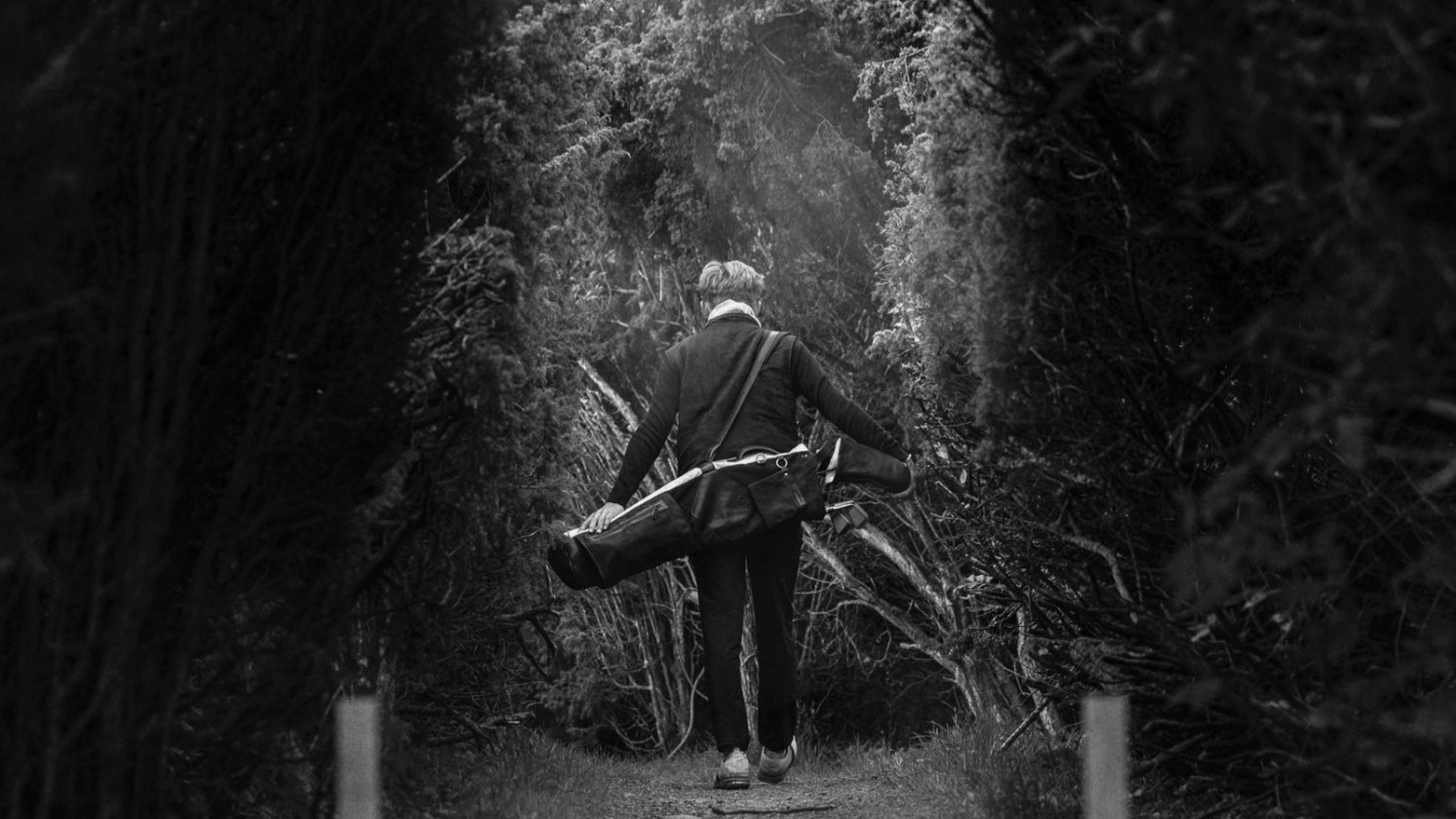 Golfer walking down a tree-lined path with a Pine Coast carry bag over the shoulder